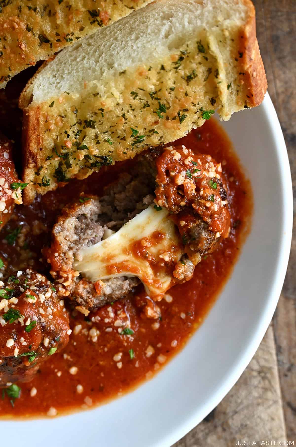A bowl containing a gooey mozzarella stuffed meatball in marinara sauce and a slice of garlic bread for dipping.