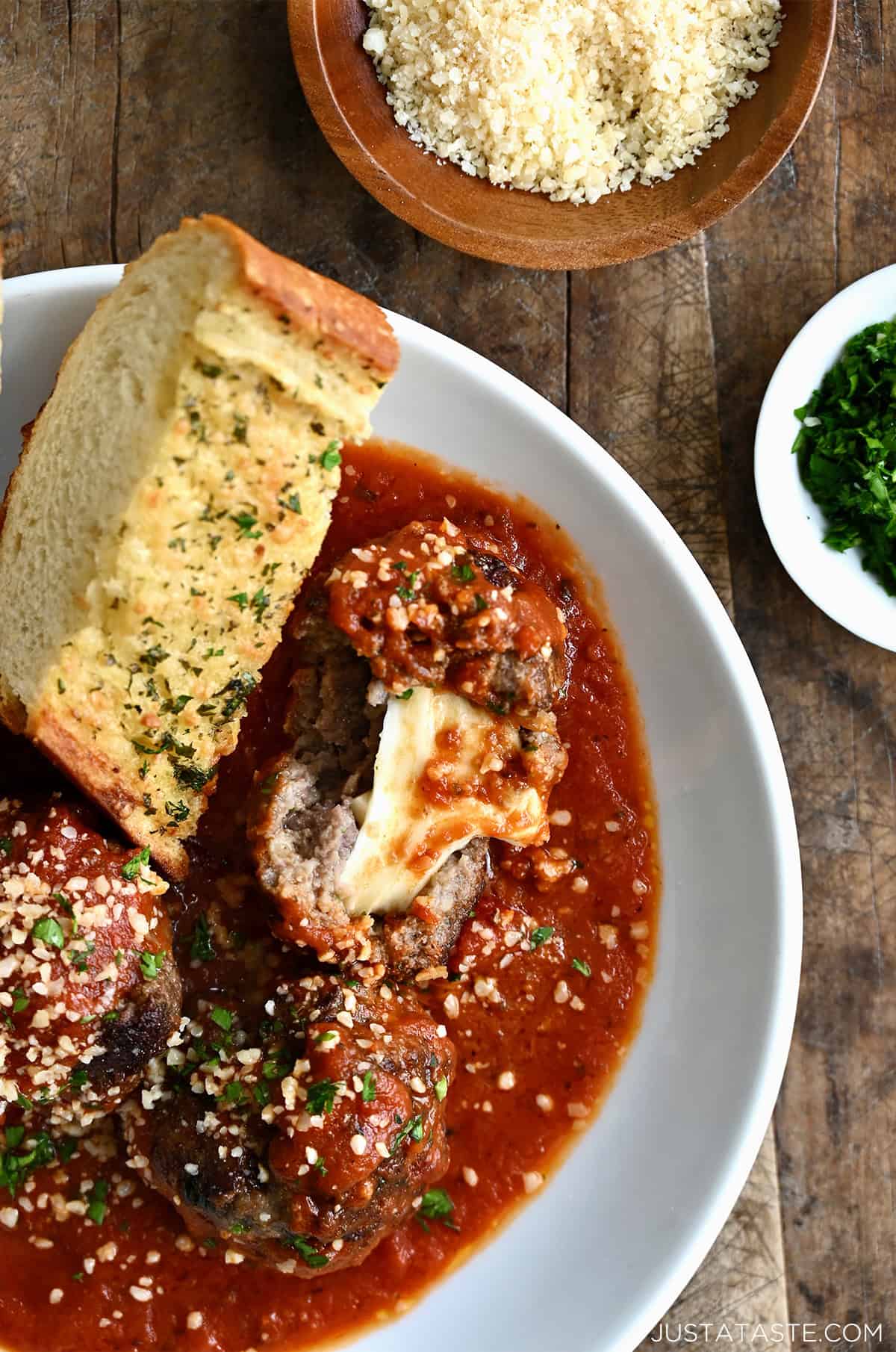 A meatball with a gooey mozzarella cheese center in a bowl with marinara sauce and a slice of crusty garlic bread.