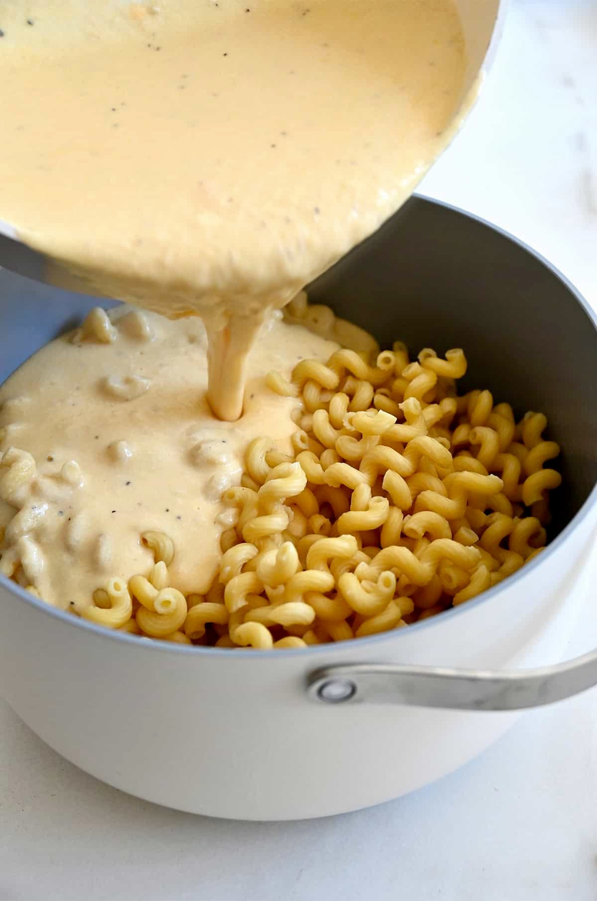 Homemade cheese sauce being poured over cavatappi pasta in a large Dutch oven.