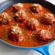 A skillet containing marinara sauce and Cheese-Stuffed Meatballs with garlic bread dippers on a plate in the background.