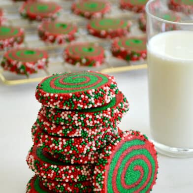 A tall stack of Christmas Pinwheel Cookies next to a glass of milk