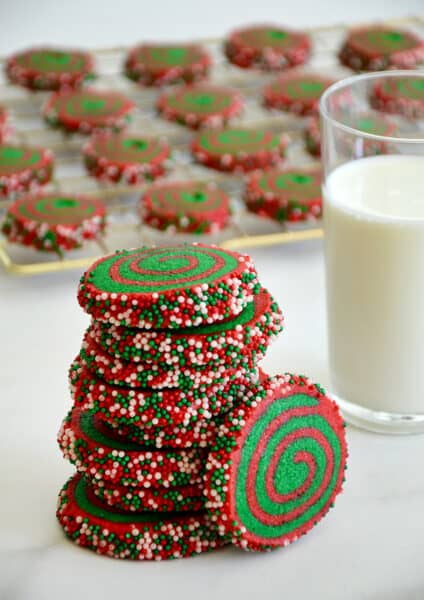 A tall stack of Christmas Pinwheel Cookies next to a glass of milk