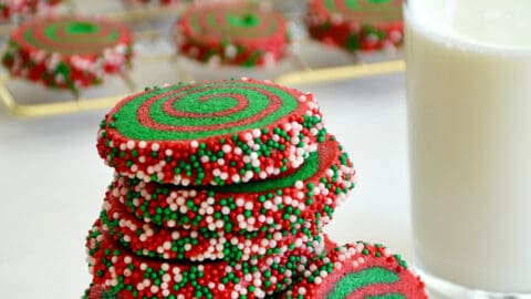 A tall stack of Christmas Pinwheel Cookies next to a glass of milk