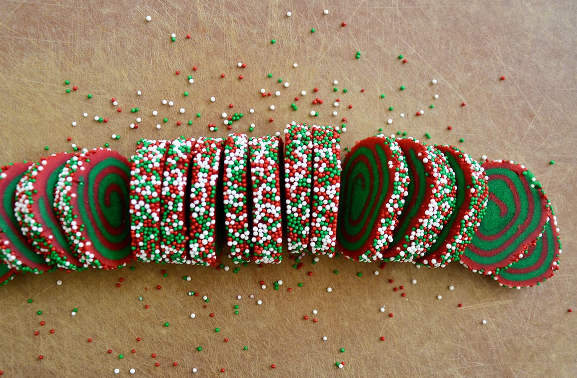 A sliced red and green cookie dough log on a cutting board