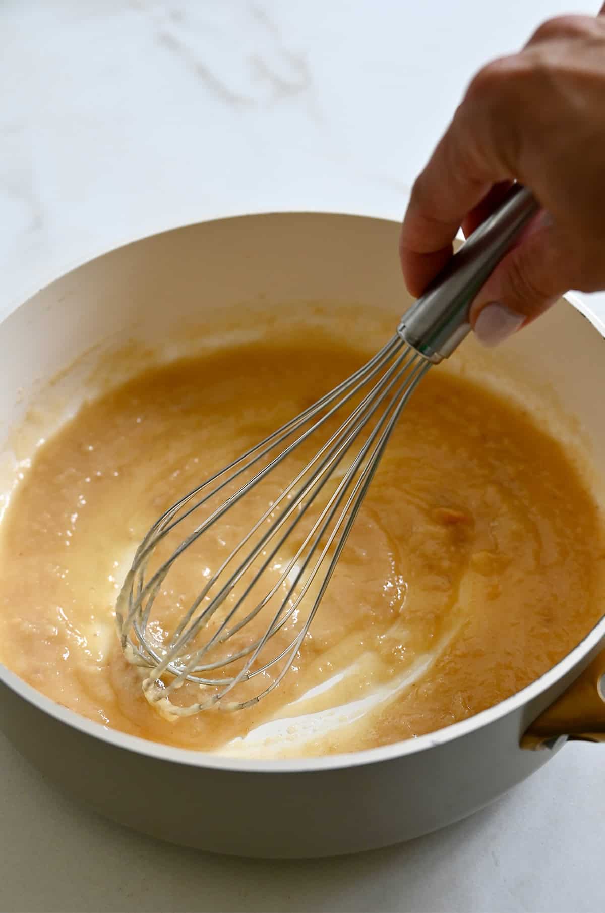 Garlic paste being whisked with flour and melted butter in a large stockpot.