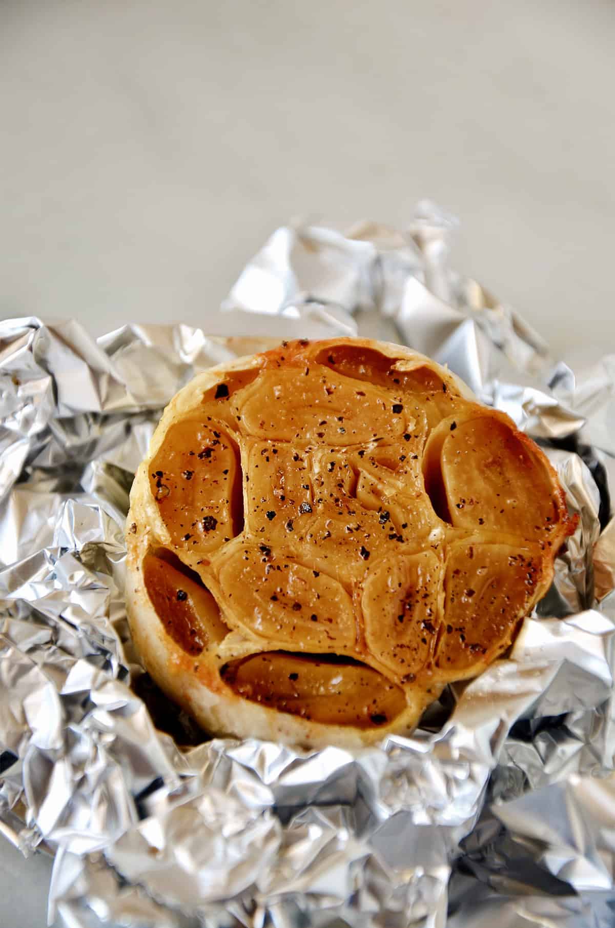 A head of roasted garlic, partially wrapped in aluminum foil.