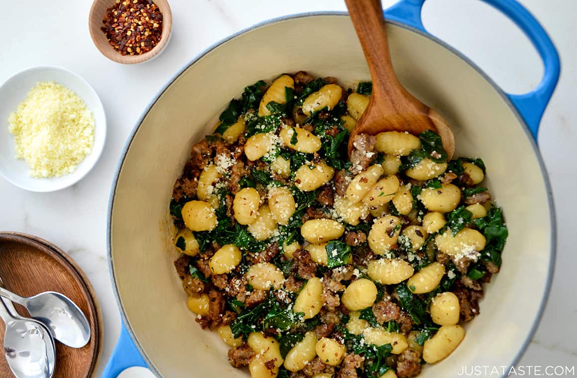 Quick A close-up view of One-Pot Gnocchi with Sausage and kale in a large stock pot next to small ramekins containing parmesan cheese and red pepper flakes