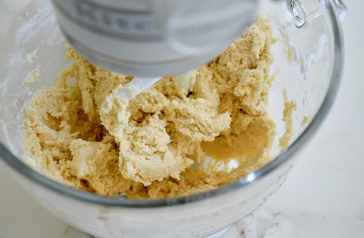 Sugar cookie dough in the bowl of a stand mixer with the paddle attachment.