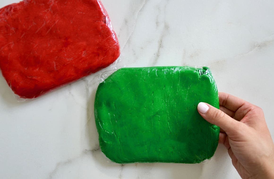 A hand holding green colored cookie dough next to red colored cookie dough