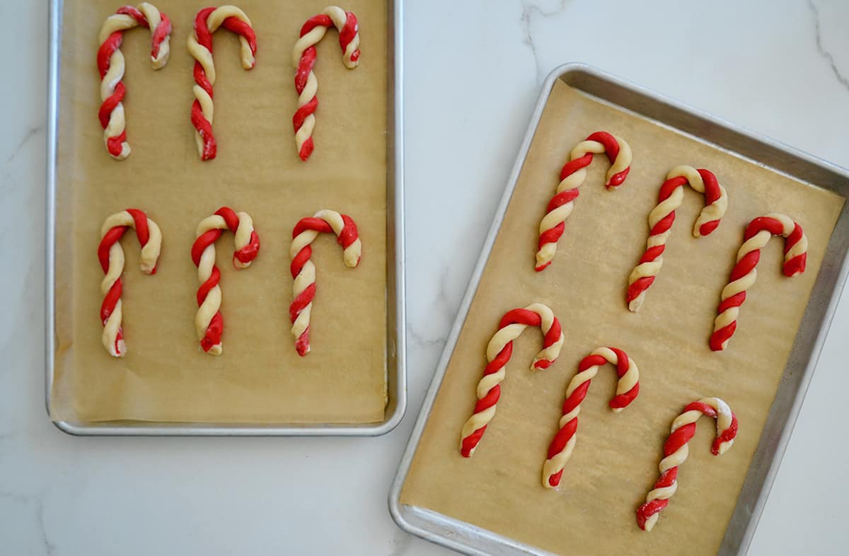 Unbaked candy cane cookies on two parchment paper-lined baking sheets.