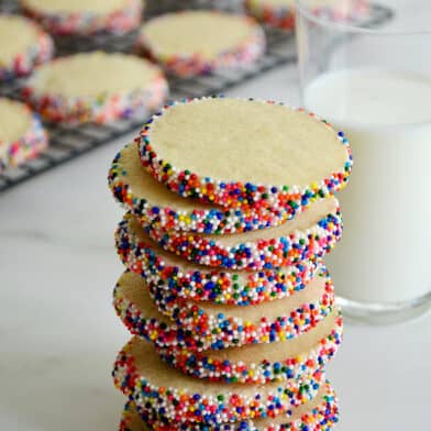 A tall stack of Slice-and-Bake Butter Cookies with rainbow sprinkles next to a glass of milk