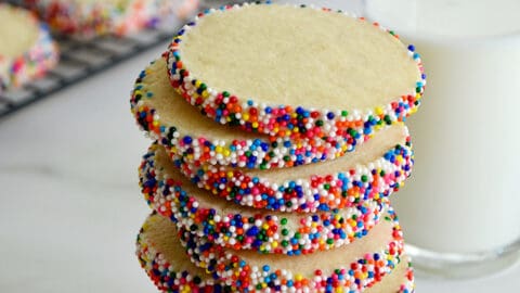 A tall stack of Slice-and-Bake Butter Cookies with rainbow sprinkles next to a glass of milk