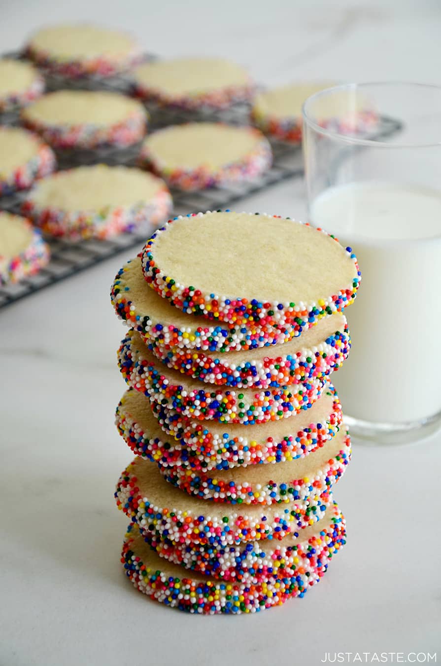 A tall stack of Slice-and-Bake Butter Cookies with rainbow sprinkles next to a glass of milk