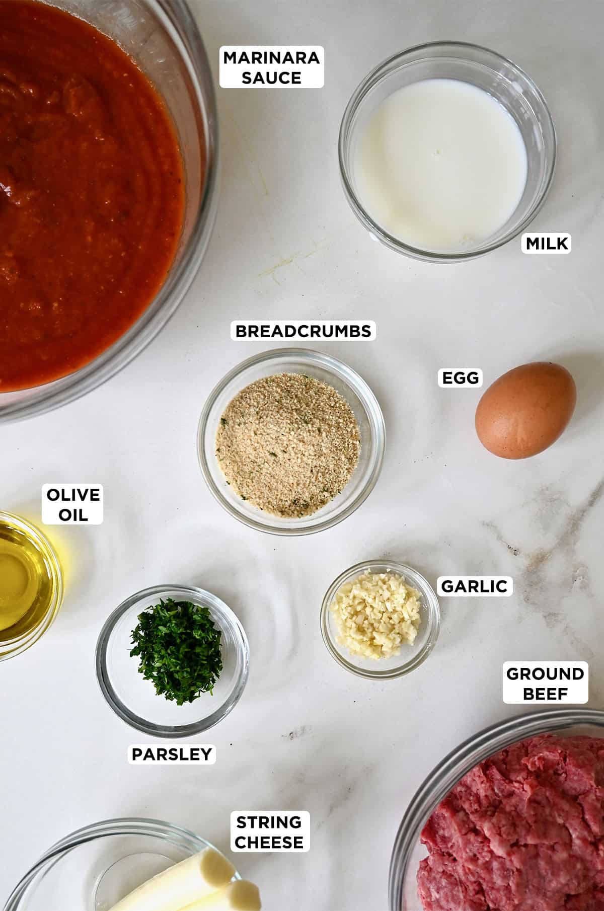 Ingredients to make meatballs stuffed with mozzarella cheese in various sizes of glass bowls.