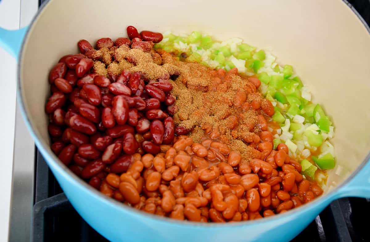 A blue dutch oven containing sautéed onions and peppers topped with kidney beans, pinto beans and seasonings.