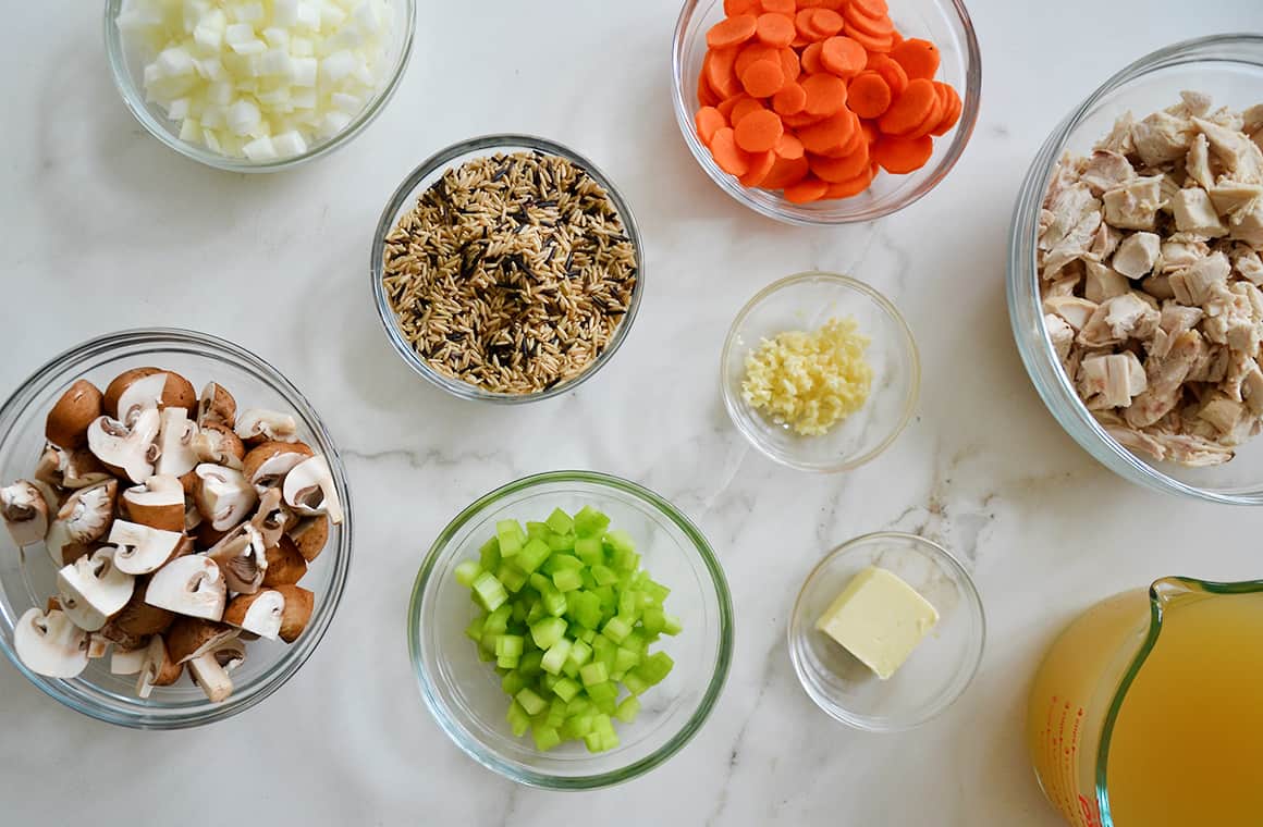 Various sizes of bowl containing chopped mushrooms, onions, wild rice, sliced carrots, cubed chicken, butter and celery