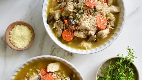 Two bowls containing homemade Chicken Wild Rice Soup next to small bowls containing parmesan and fresh herbs