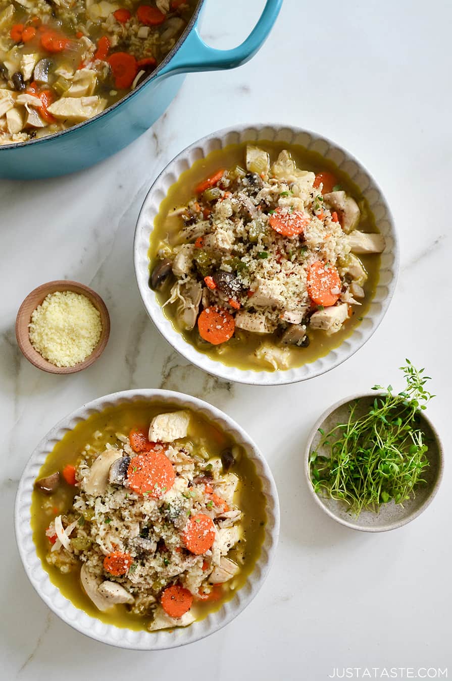 Two bowls containing homemade Chicken Wild Rice Soup next to small bowls containing parmesan and fresh herbs