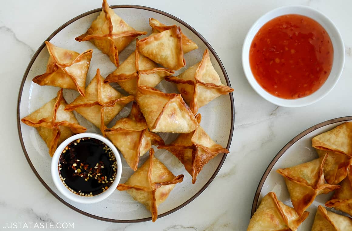 A plate piled with crispy Cream Cheese Wontons and a small bowl of soy sauce next to a bowl filled with sweet chili sauce