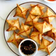 A top-down view of a plate piled high with Air Fryer Cream Cheese Wontons along with a small bowl containing soy dipping sauce. A bowl filled with sweet chili sauce is next to the plate.