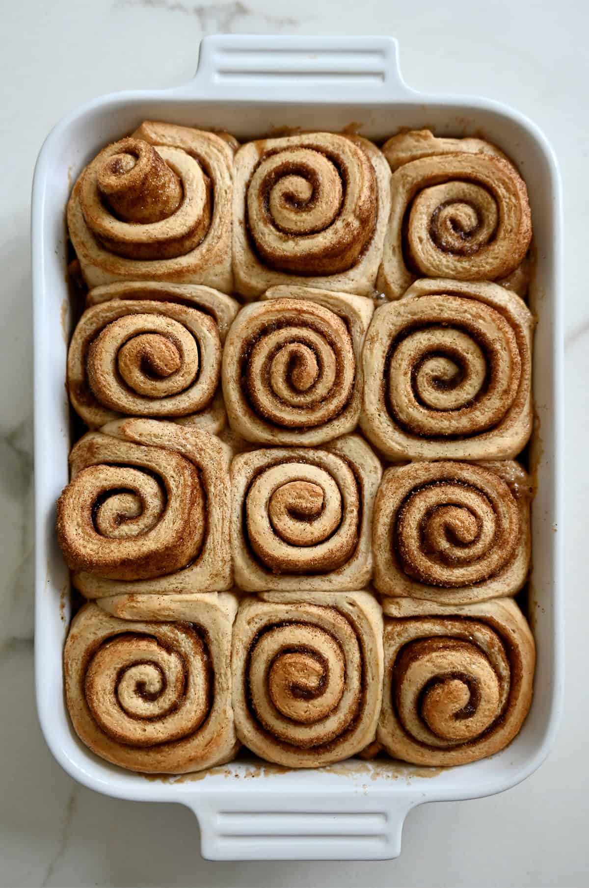 Baked maple pecan sticky buns in a baking dish before being flipped over to expose the gooey topping.