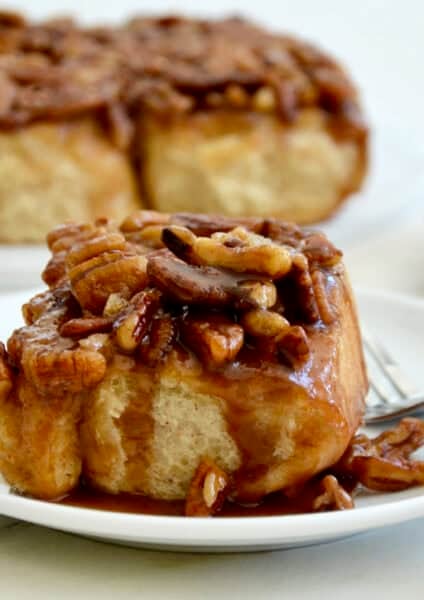 A freshly baked maple pecan sticky bun on a plate with a fork.