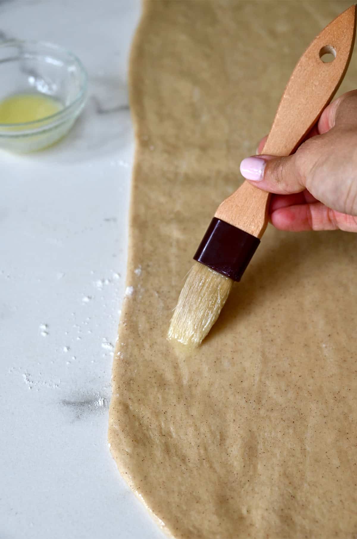 Brushing melted butter onto sticky bun dough.