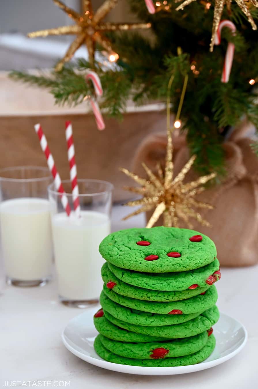 A tall stack of Cake Mix Grinch Cookies on a plate in front of two glasses of milk with straws