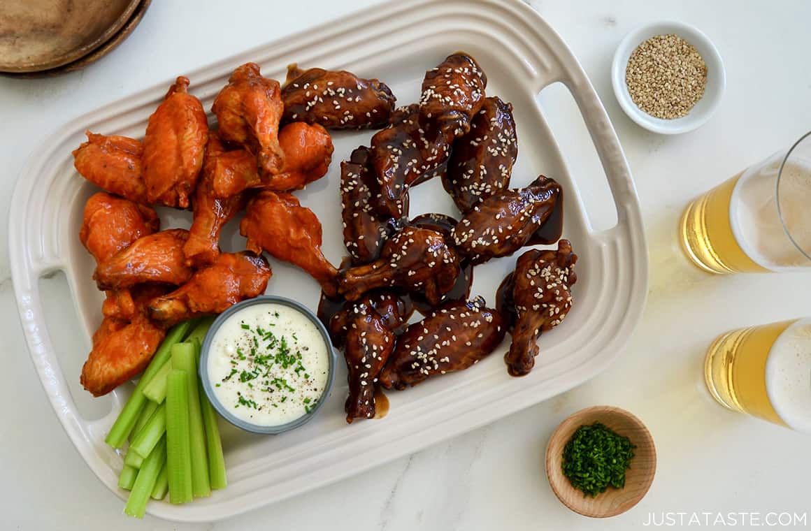 Two different flavors of Air Fryer Chicken Wings on a plate with celery and a small ramekin of ranch dressing next to two glasses filled with beer