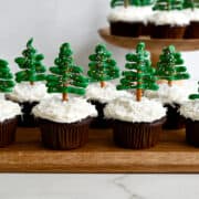 Chocolate Christmas Tree Cupcakes with cream cheese frosting and coconut "snow" on a wooden serving board.