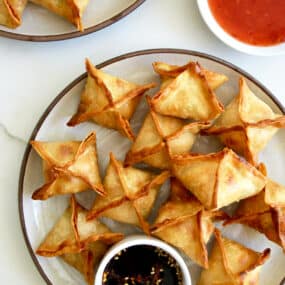 Air Fryer Cream Cheese Wontons on a plate with a small ramekin containing soy sauce next to a small bowl containing sweet chili sauce