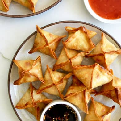 Air Fryer Cream Cheese Wontons on a plate with a small ramekin containing soy sauce next to a small bowl containing sweet chili sauce