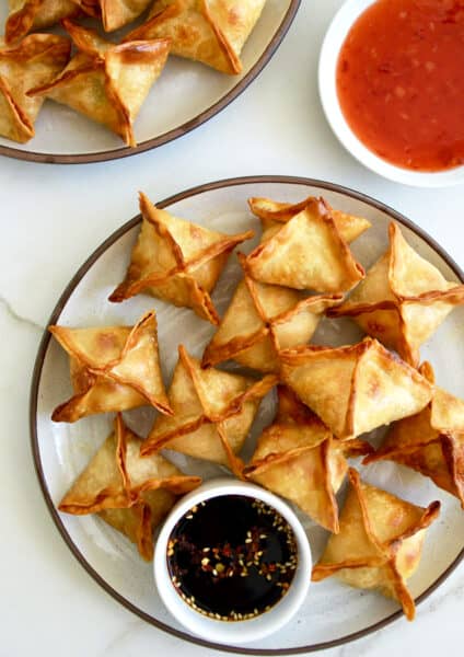Air Fryer Cream Cheese Wontons on a plate with a small ramekin containing soy sauce next to a small bowl containing sweet chili sauce