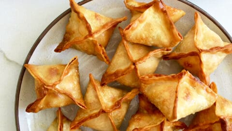 Air Fryer Cream Cheese Wontons on a plate with a small ramekin containing soy sauce next to a small bowl containing sweet chili sauce