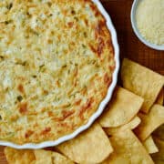 Hot and Creamy Artichoke Dip in a white baking dish surrounded by tortilla chips.