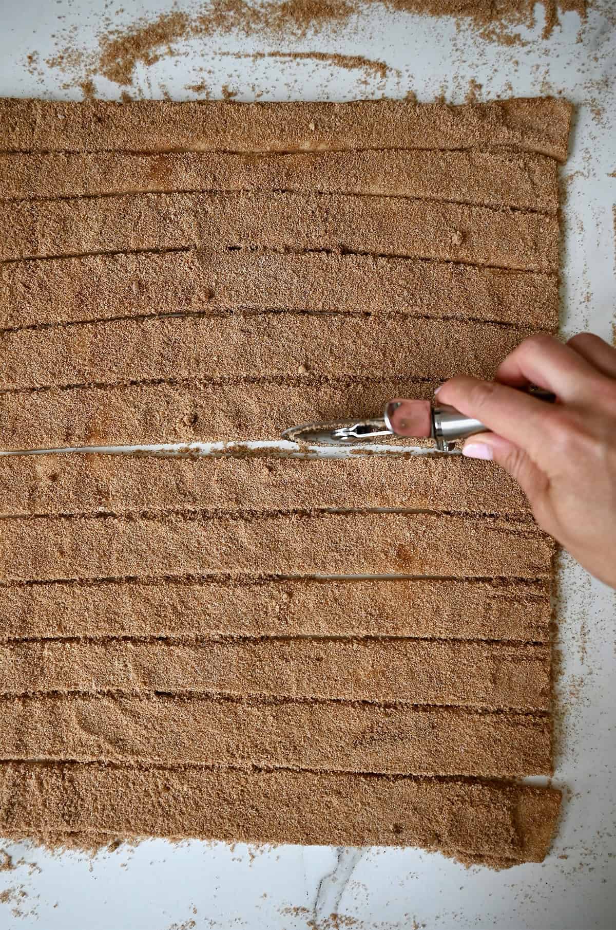 Using a pizza cutter to slice cinnamon sugar-topped dough into strips.