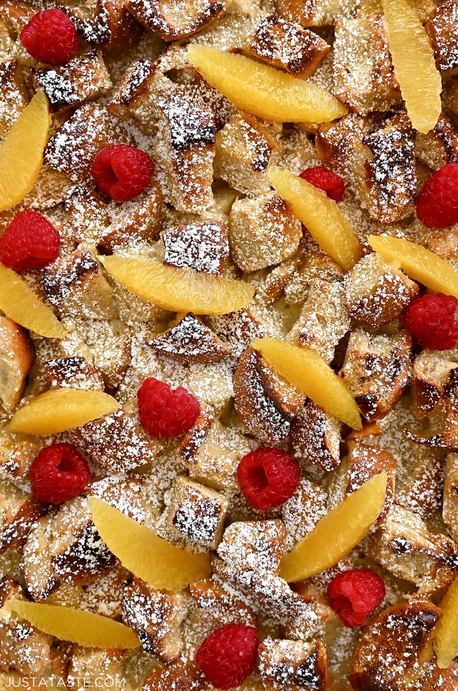 A close-up view of the best French Toast Casserole dusted with powdered sugar and topped with orange slices and fresh raspberries