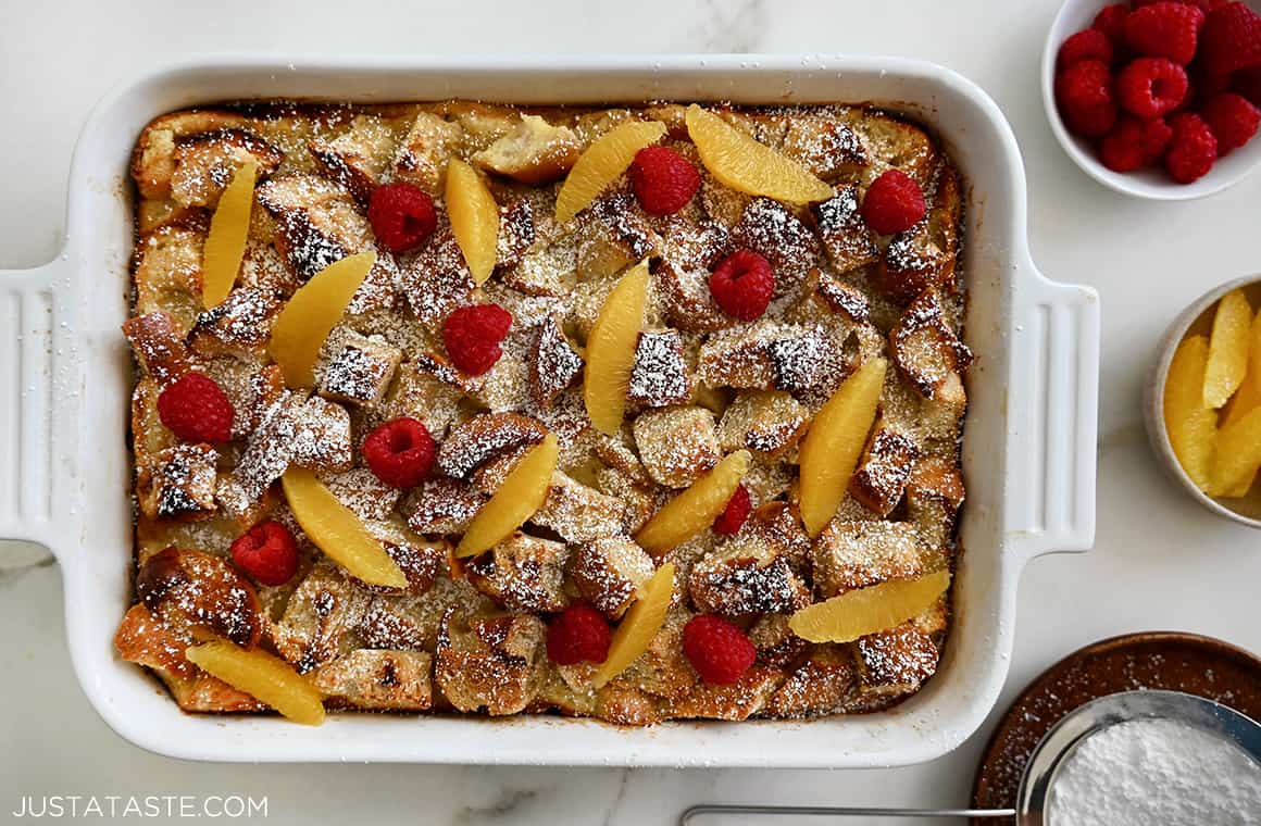 A top-down view of white baking dish containing homemade Overnight French Toast Bake dusted with powdered sugar and topped with fresh fruit