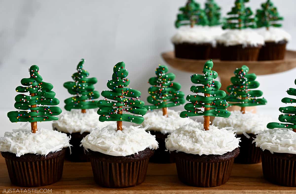 Two rows of chocolate Christmas tree cupcakes with cream cheese frosting, shredded coconut "snow" and candy melt Christmas tree toppers.