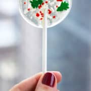 A hand holding a homemade lollipop with holiday sprinkles.