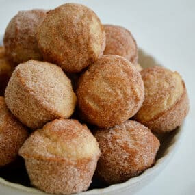 A white bowl piled high with Mini Sour Cream Doughnut Muffins