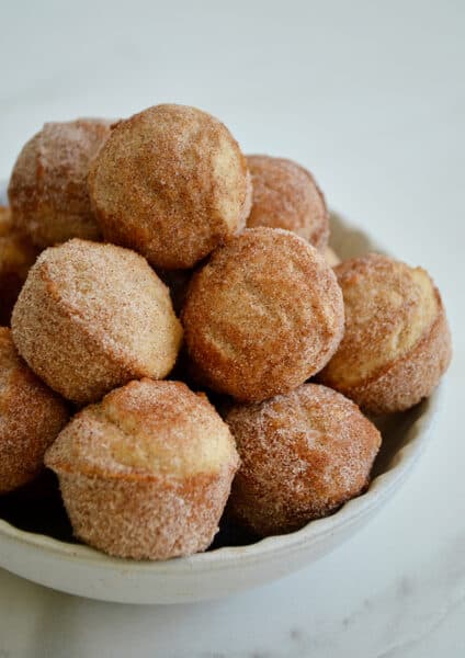 A white bowl piled high with Mini Sour Cream Doughnut Muffins