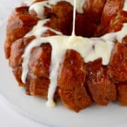 Cream cheese frosting being poured over monkey bread made from canned biscuits.