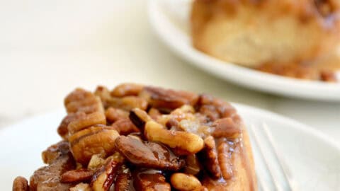A maple pecan sticky bun with gooey caramel sauce on a plate with a fork.