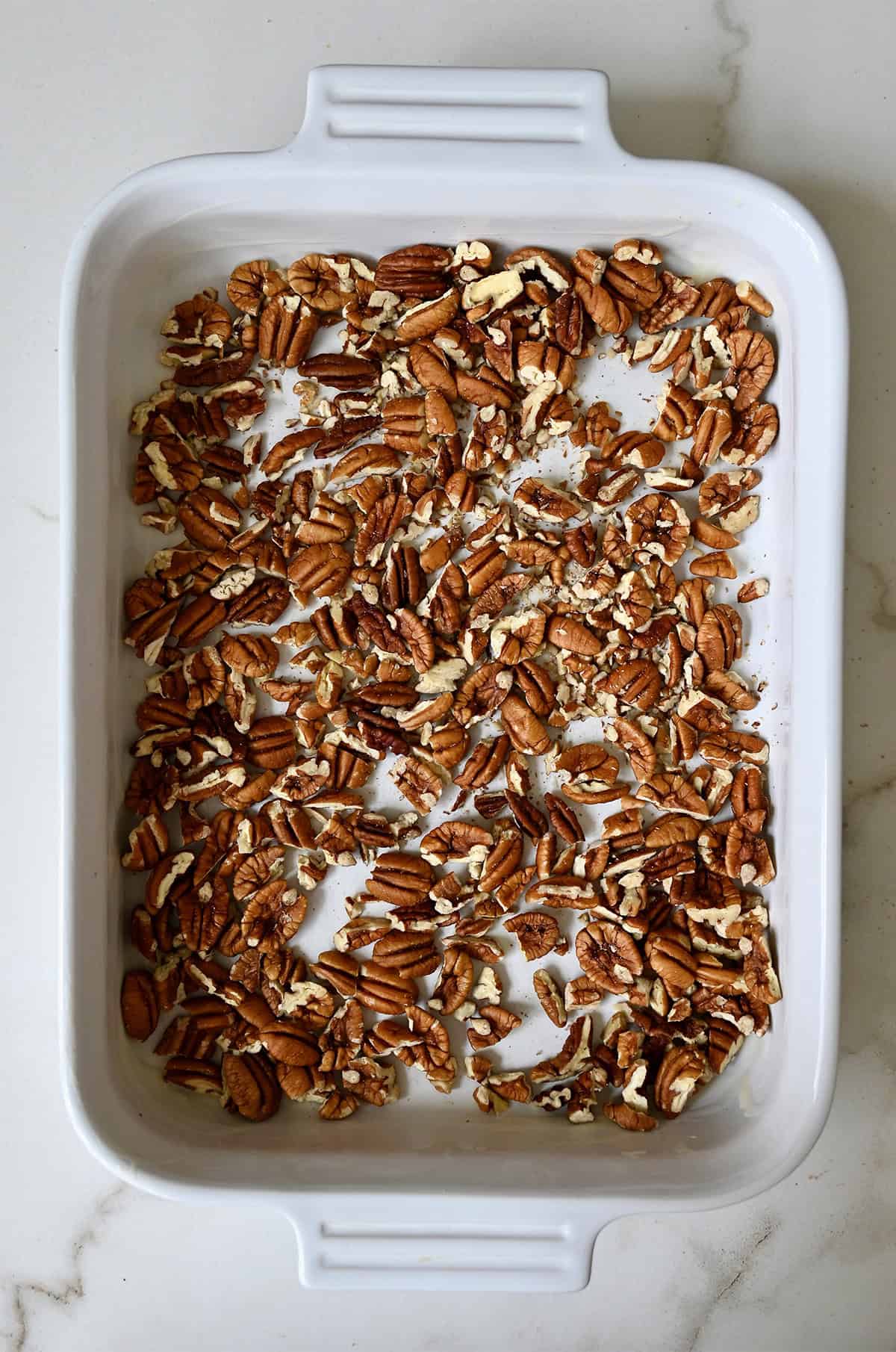 Pecans are scattered in a 9x13 baking dish.