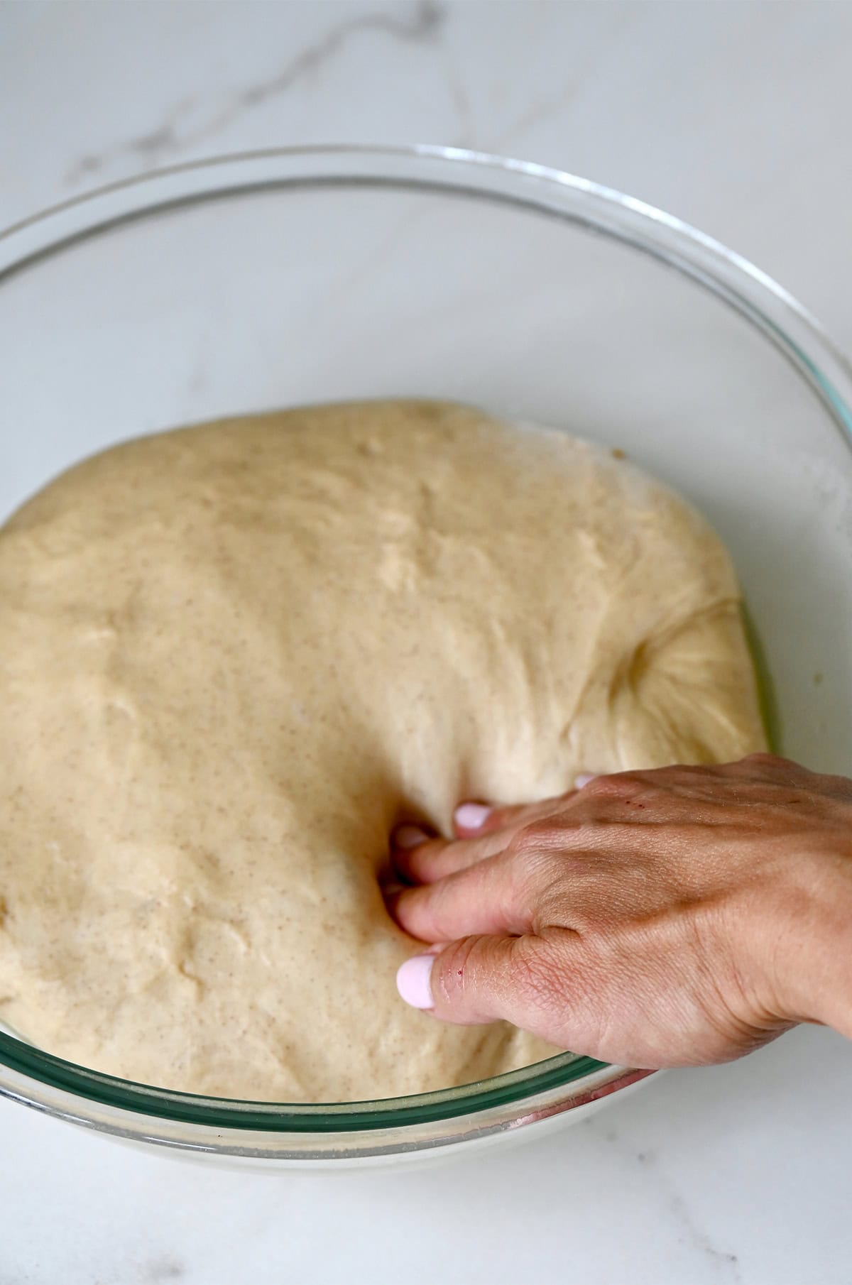 A hand presses into proofed sticky bun dough in a greased bowl.