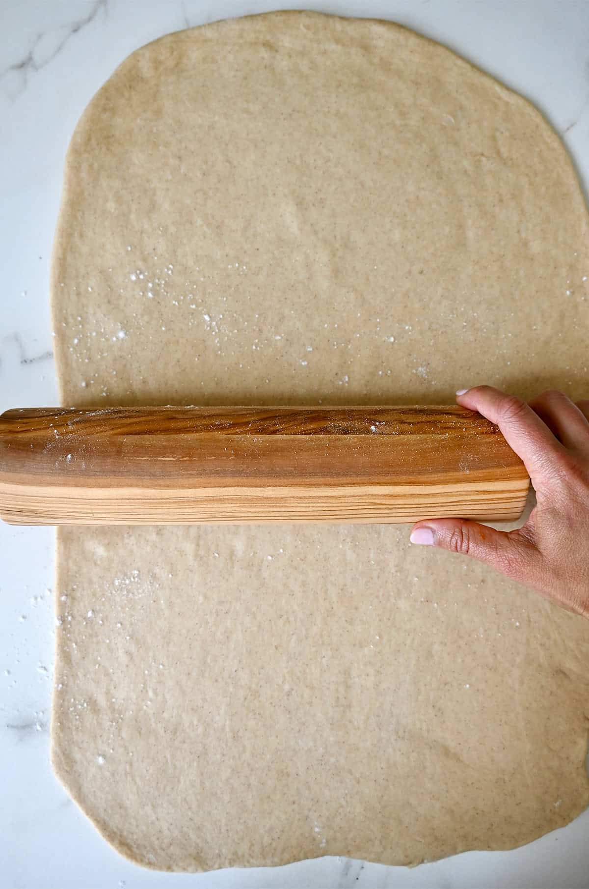 Using a wooden rolling pin to roll out sticky bun dough.