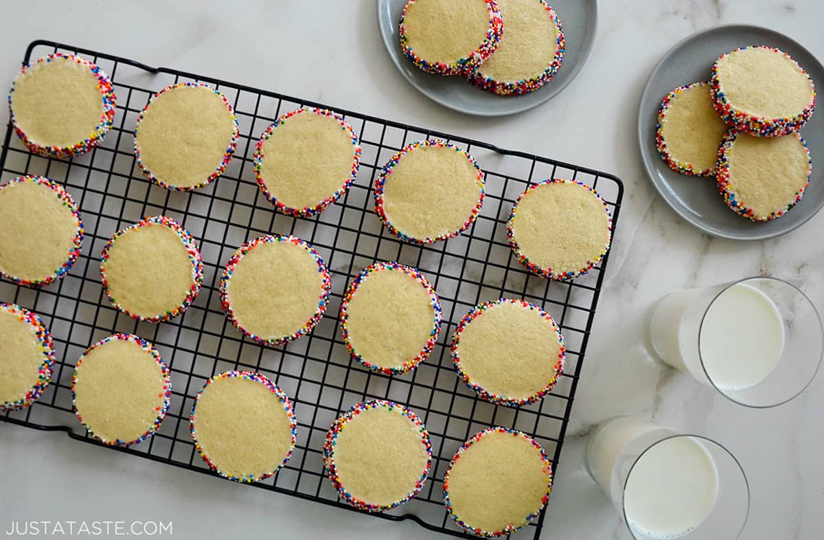 Slice-and-Bake Butter Cookies studded with rainbow sprinkles on a wire cooling rack next to two glasses of milk.