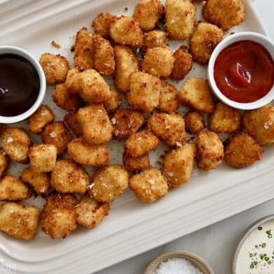 A white platter containing air fryer chicken nuggets with small bowls of dipping sauces.