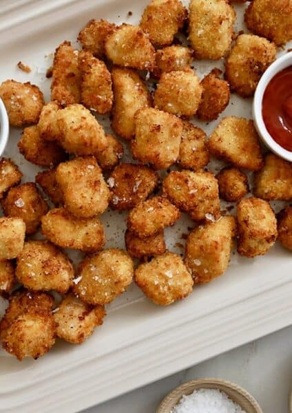 A white platter containing air fryer chicken nuggets with small bowls of dipping sauces.